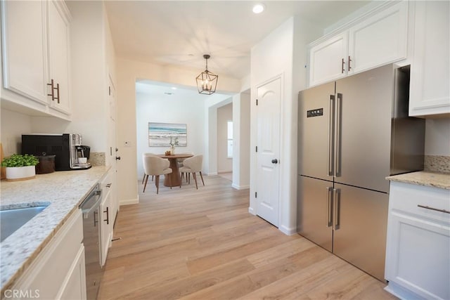 kitchen with appliances with stainless steel finishes, white cabinets, light stone counters, and decorative light fixtures