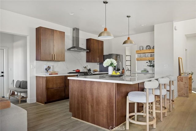 kitchen with appliances with stainless steel finishes, pendant lighting, tasteful backsplash, light wood-type flooring, and wall chimney exhaust hood