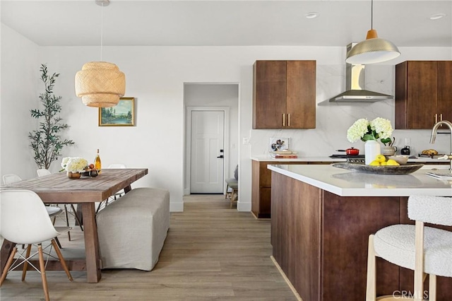 kitchen with decorative light fixtures, light wood-type flooring, a kitchen breakfast bar, decorative backsplash, and wall chimney range hood