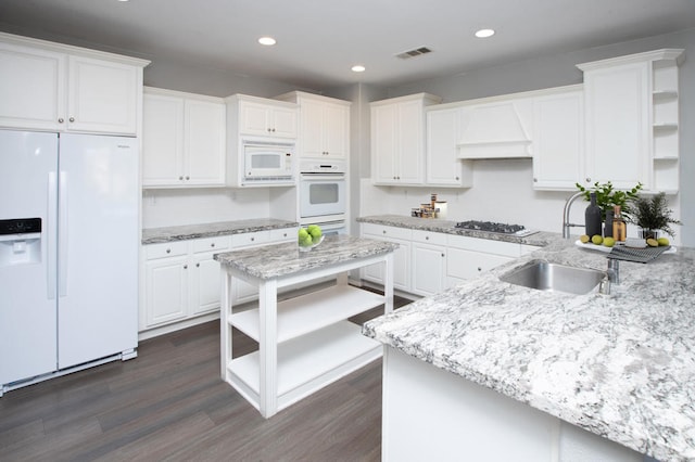 kitchen featuring custom exhaust hood, white appliances, white cabinetry, light stone countertops, and dark wood-type flooring