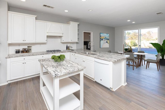 kitchen with white cabinetry, stainless steel gas cooktop, white dishwasher, custom range hood, and sink