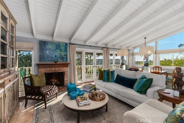 sunroom / solarium featuring a wealth of natural light, vaulted ceiling with beams, a tiled fireplace, and french doors