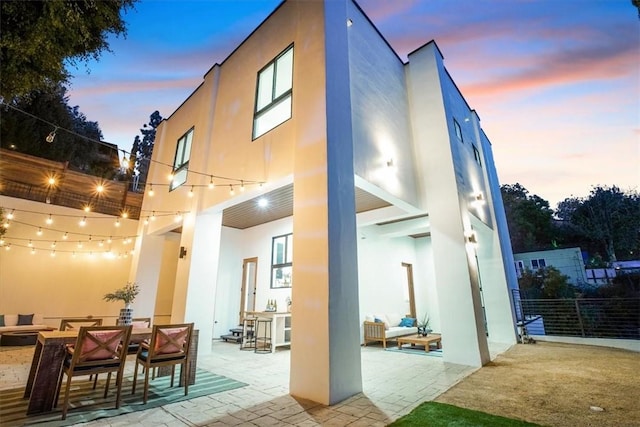 back house at dusk featuring exterior bar and a patio area