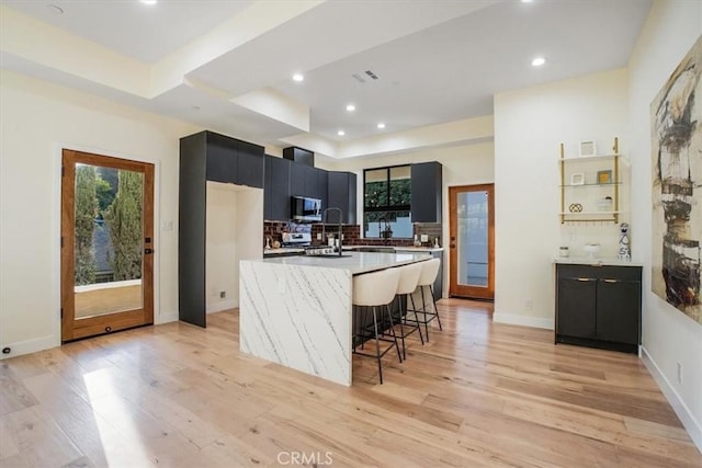 kitchen with a breakfast bar, appliances with stainless steel finishes, an island with sink, and light hardwood / wood-style floors