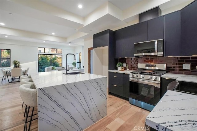 kitchen with a kitchen bar, a center island with sink, stainless steel appliances, backsplash, and sink