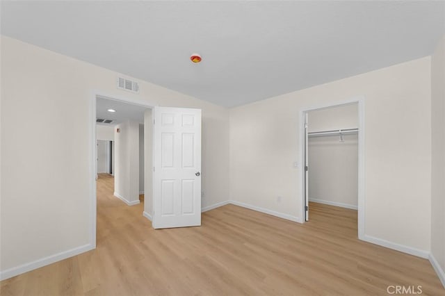 unfurnished bedroom featuring a closet, a walk in closet, and light hardwood / wood-style floors