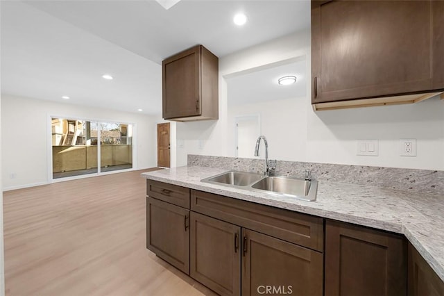 kitchen featuring light stone countertops, sink, dark brown cabinets, and light wood-type flooring