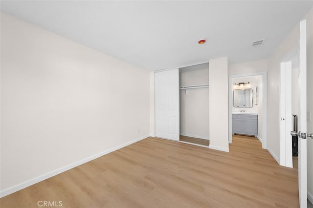 unfurnished bedroom featuring a closet, sink, connected bathroom, and light hardwood / wood-style floors