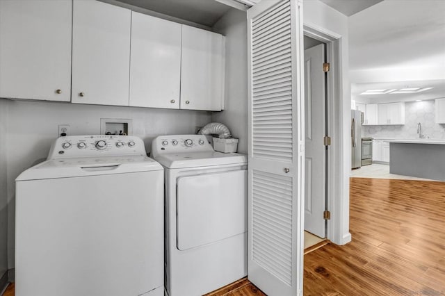 laundry area with cabinets, light hardwood / wood-style floors, washing machine and clothes dryer, and sink