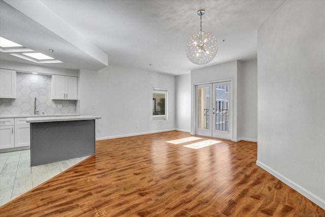 unfurnished living room featuring a skylight, french doors, an inviting chandelier, light hardwood / wood-style floors, and sink