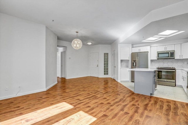 kitchen with appliances with stainless steel finishes, a center island, decorative light fixtures, white cabinetry, and tasteful backsplash