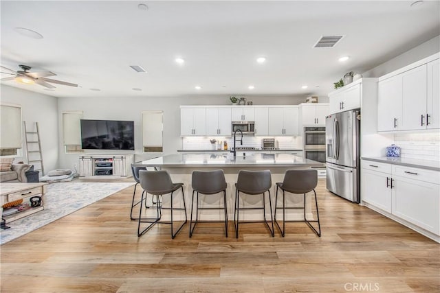 kitchen featuring visible vents, appliances with stainless steel finishes, a breakfast bar, open floor plan, and light wood-type flooring