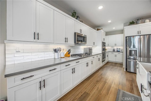 kitchen with decorative backsplash, white cabinetry, light hardwood / wood-style flooring, and stainless steel appliances