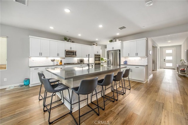 kitchen featuring visible vents, appliances with stainless steel finishes, an island with sink, light wood-type flooring, and a kitchen bar