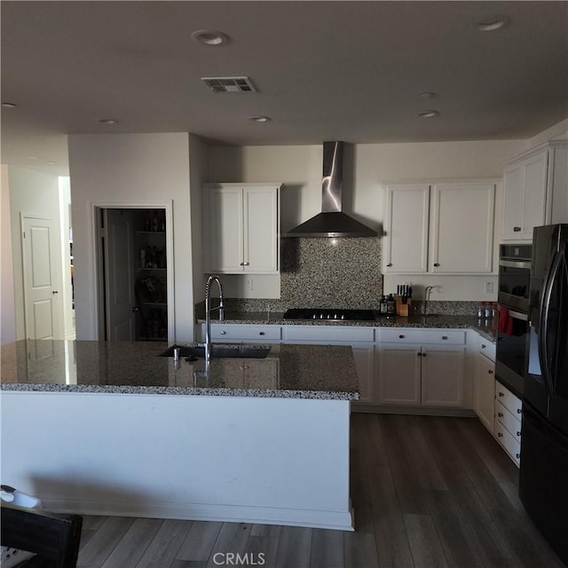 kitchen with black appliances, white cabinetry, wall chimney range hood, sink, and a kitchen island with sink