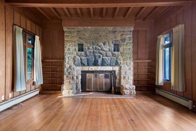 unfurnished living room featuring baseboard heating, wood ceiling, wood walls, and a stone fireplace