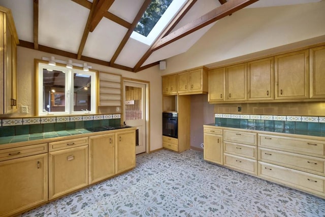 kitchen with tile counters, black oven, a skylight, tasteful backsplash, and high vaulted ceiling