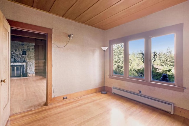 unfurnished room featuring baseboard heating, wood ceiling, a fireplace, and hardwood / wood-style floors