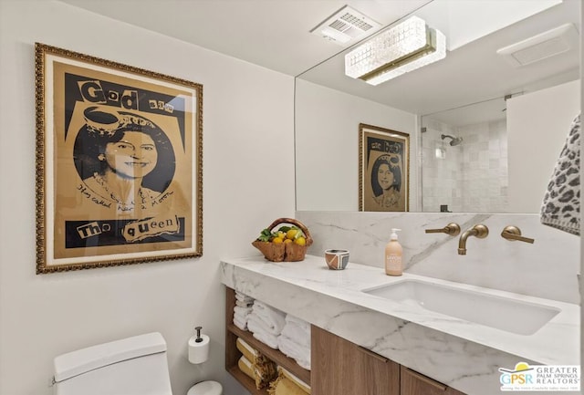 bathroom with toilet, a tile shower, and vanity