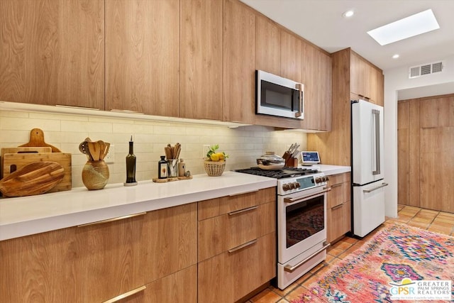 kitchen featuring decorative backsplash, premium appliances, a skylight, and light tile patterned flooring