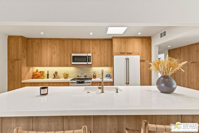 kitchen with backsplash, a kitchen bar, sink, high end appliances, and a skylight