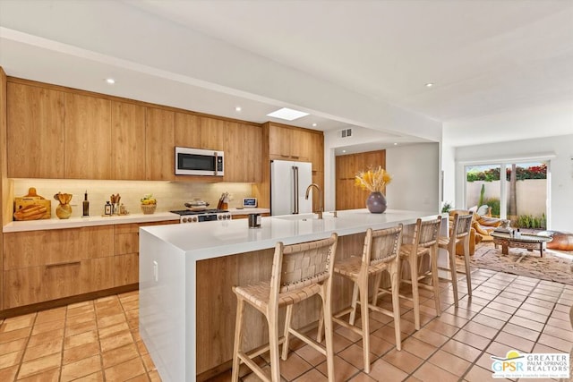 kitchen with backsplash, a kitchen island with sink, high end fridge, light tile patterned floors, and stove