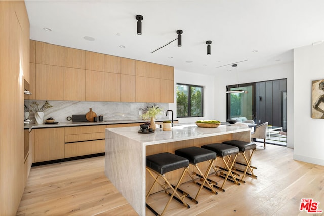 kitchen featuring light brown cabinetry, light hardwood / wood-style floors, backsplash, and a kitchen island with sink