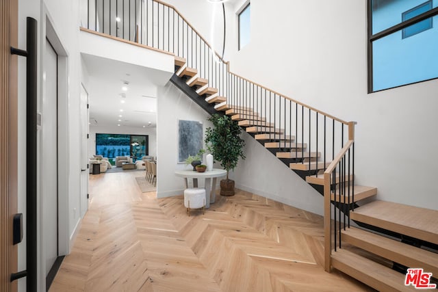 stairway featuring plenty of natural light, a high ceiling, and parquet flooring