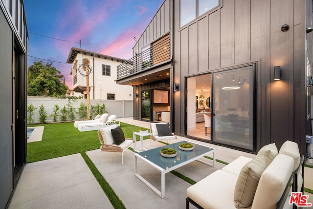 patio terrace at dusk with a balcony, a lawn, and an outdoor hangout area