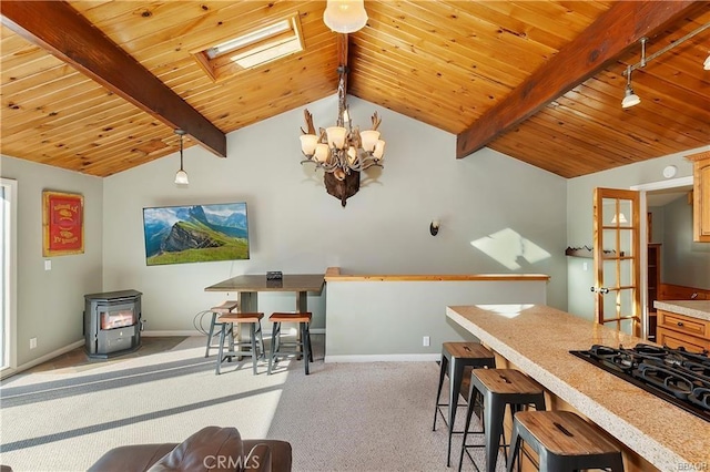 kitchen featuring black gas stovetop, light colored carpet, pendant lighting, wood ceiling, and a wood stove