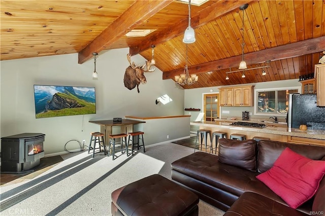 living room with vaulted ceiling with beams, a wood stove, a chandelier, wooden ceiling, and dark carpet