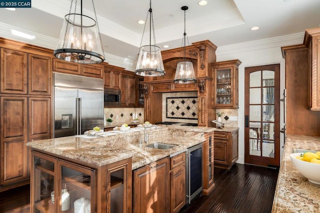 kitchen featuring tasteful backsplash, a tray ceiling, decorative light fixtures, built in appliances, and sink