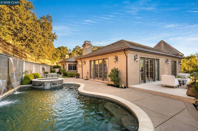 rear view of property with a swimming pool with hot tub, pool water feature, french doors, and a patio