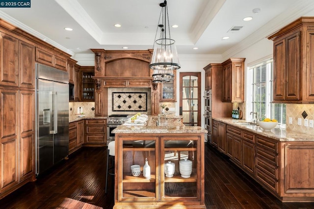 kitchen featuring pendant lighting, premium appliances, a center island with sink, and tasteful backsplash