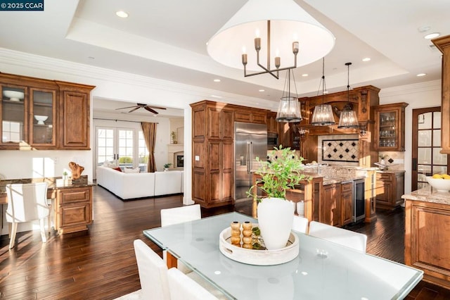 dining space with ceiling fan with notable chandelier, beverage cooler, dark hardwood / wood-style floors, a tray ceiling, and crown molding