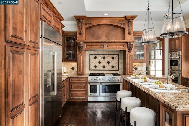 kitchen with decorative backsplash, decorative light fixtures, dark wood-type flooring, high quality appliances, and light stone counters