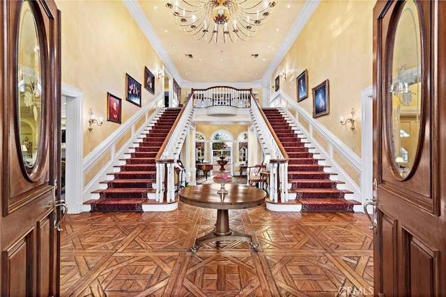 foyer entrance featuring a high ceiling, parquet flooring, ornamental molding, and a notable chandelier