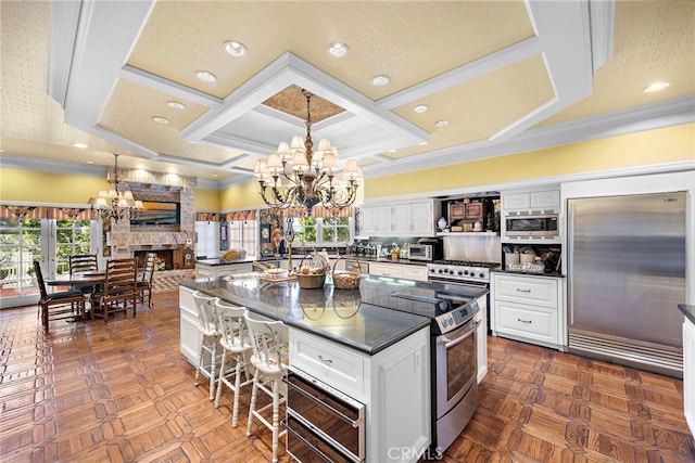 kitchen featuring white cabinetry, coffered ceiling, a stone fireplace, built in appliances, and pendant lighting