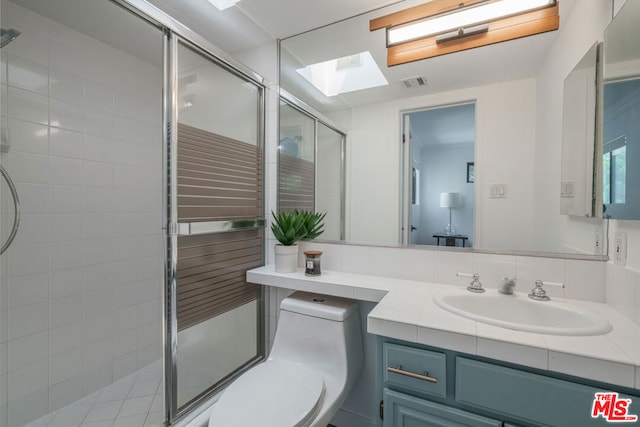 bathroom featuring a shower with door, a skylight, vanity, and toilet