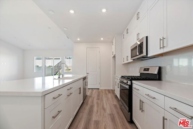 kitchen with sink, light wood-type flooring, appliances with stainless steel finishes, an island with sink, and white cabinets