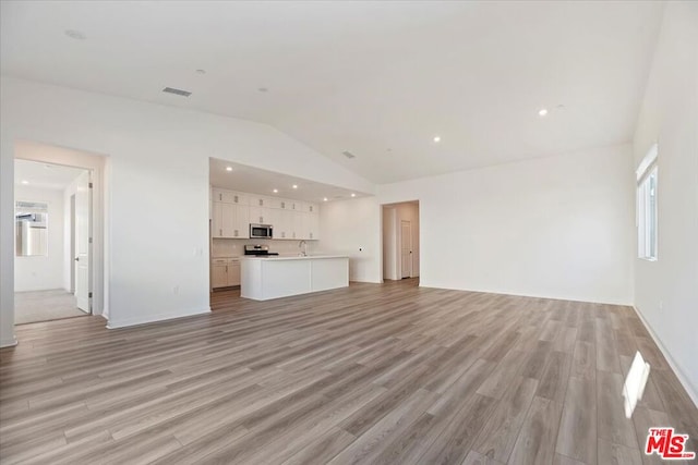 unfurnished living room with lofted ceiling, sink, and light hardwood / wood-style floors