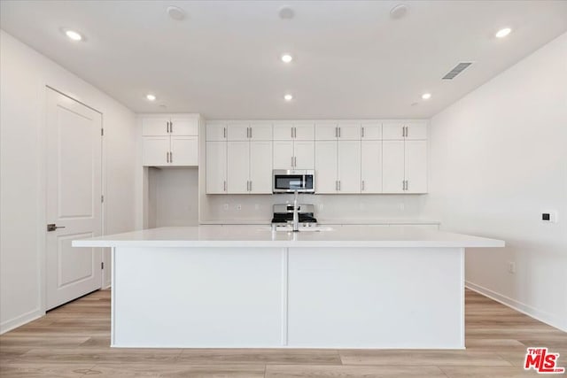 kitchen with a large island, light hardwood / wood-style flooring, white cabinets, and appliances with stainless steel finishes