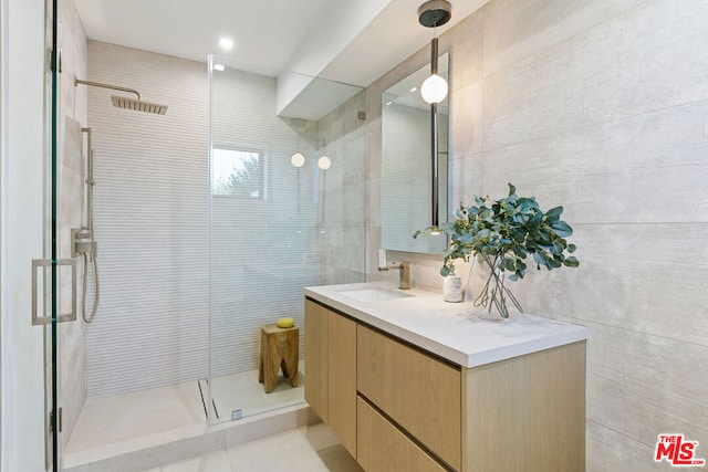 bathroom with a shower with shower door, vanity, and tile walls