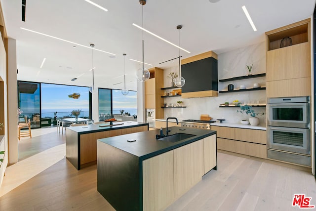 kitchen with stainless steel double oven, sink, light wood-type flooring, floor to ceiling windows, and a center island with sink