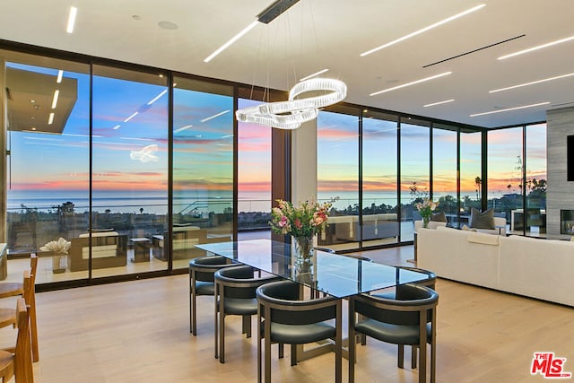 dining room featuring a water view, expansive windows, a notable chandelier, and light hardwood / wood-style flooring