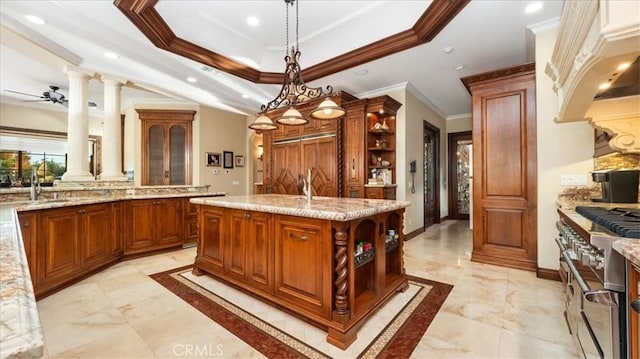 kitchen featuring a kitchen island with sink, hanging light fixtures, decorative columns, a tray ceiling, and high end stainless steel range