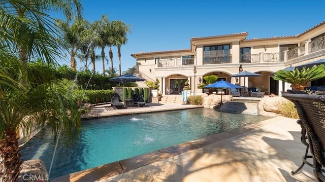 rear view of house with pool water feature, a patio, and a balcony