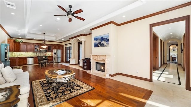 living room with ceiling fan, a high end fireplace, a tray ceiling, and light wood-type flooring