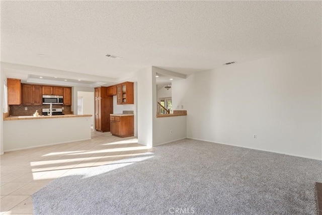 unfurnished living room with a raised ceiling, light colored carpet, and a textured ceiling