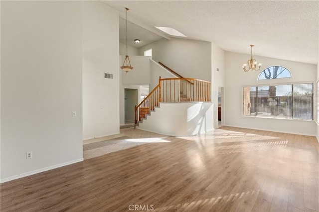 unfurnished living room featuring a notable chandelier, beam ceiling, light wood-type flooring, a skylight, and high vaulted ceiling